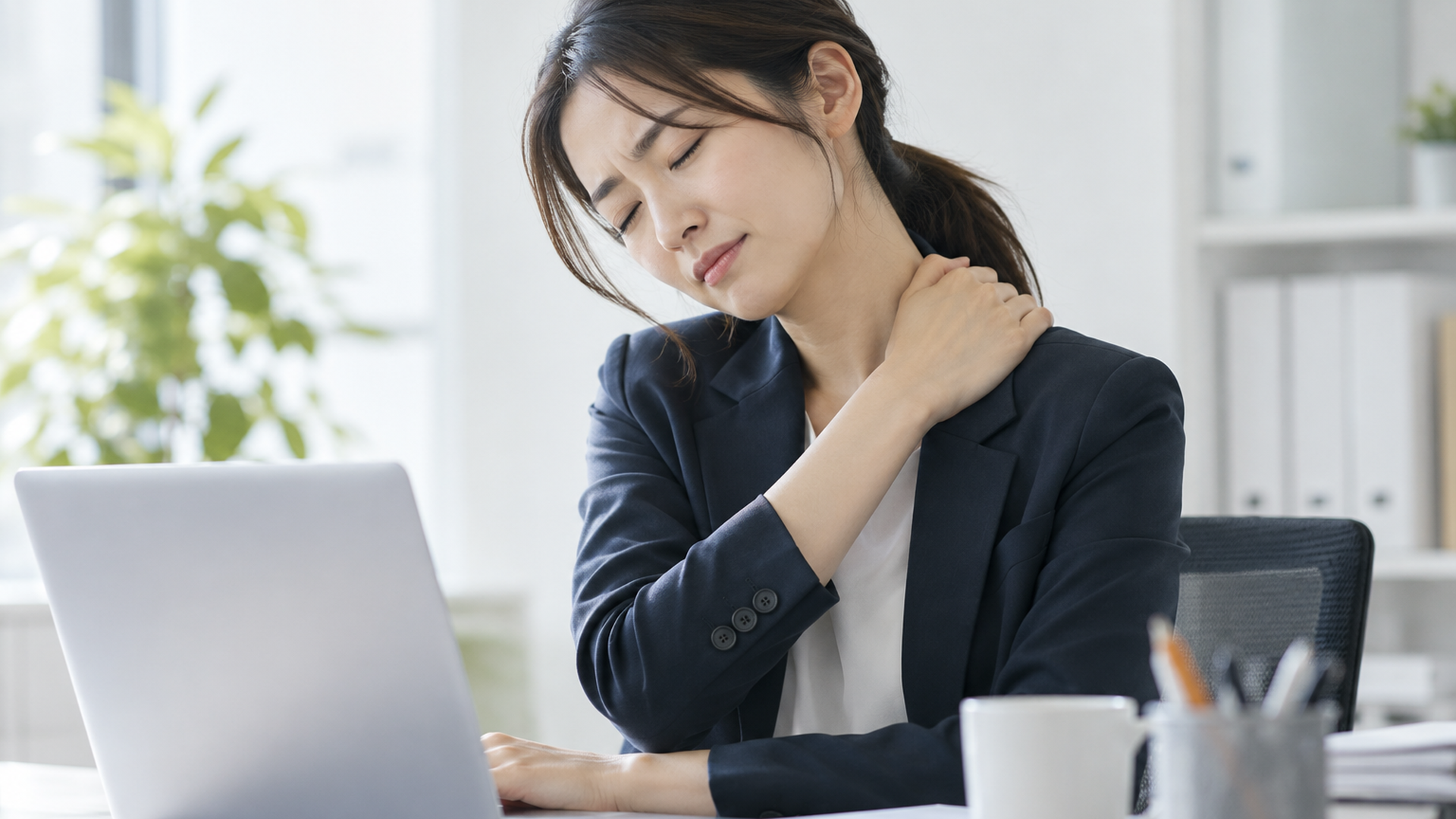 デスクワーク中に首や肩をこわばらせる会社員のリアルな写真